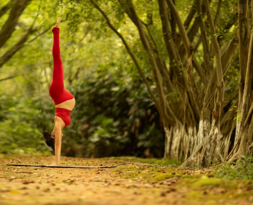 a pregnant woman doing hand stand beside green trees